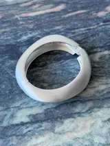 Pulsera rígida de metal plateado con forma oval irregular y acabado mate.