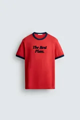 Camiseta de corte regular color rojo con cuello redondo y bordes de mangas en color azul marino. Presenta una estampa frontal con la frase 'The Best Plan.' en color azul marino.