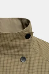 Cazadora reversible de cuello subido y manga larga, con bolsillos delanteros y cierre frontal cruzado con botones negros. Diseño de cuadros en tonos tostados.