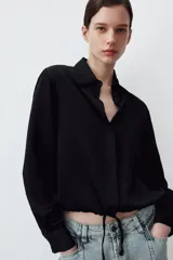 Camisa de satén con cuello solapa, manga larga con puños y bajo ajustable mediante cordones. Presenta cierre frontal con botones ocultos.