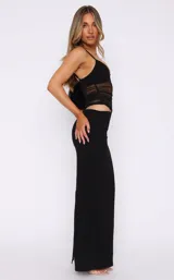 Vestido largo negro de tirantes finos, con escote corazón y detalle de transparencias en el torso con bandas horizontales de tela opaca. La falda es ajustada y presenta un corte en la cadera.