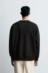 Sudadera negra de corte relaxed fit, confeccionada en tejido técnico interlock de algodón con elasticidad. Presenta cuello redondo, manga larga y una etiqueta aplicada en el bajo. Los acabados son en rib.