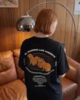Remera negra de corte oversize con estampado gráfico en la espalda que incluye ilustraciones de carpinchos sobre una cuadrícula y texto descriptivo en color blanco y naranja.