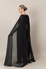 Vestido largo de crepe negro, con capa de gasa que sale de los hombros y abertura en la espalda.