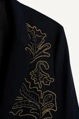 Blazer de corte relajado confeccionada en tejido con lana, color negro. Presenta cuello con solapas de muesca, cierre frontal de un botón y bolsillos de plastrón en la cadera. Destaca por su bordado en hilo dorado con motivos vegetales en la parte frontal.
