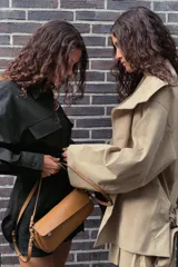 Trench color beige con cuello de solapa subido y manga larga. Tiene bolsillos laterales, forro interior y cinturón de lazo en el mismo tejido. El cuello se cierra con un botón.