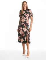 Vestido midi de satén con estampado floral sobre fondo negro. Presenta cuello a la base con frunce, mangas cortas abullonadas con terminación elástica, cintura definida y un tajo lateral pronunciado. Incluye forro interno y lazo posterior para ajustar el cuello.