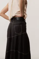 Falda larga de lino color beige, de corte asimétrico con costuras decorativas pespunteadas en contraste y diseño envolvente con bajo más largo en la parte trasera.