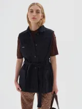 Chaleco de jean negro, con cuello camisero, cierre frontal de botones, dos bolsillos con solapa en el pecho y dos bolsillos de parche en la parte inferior. Incluye tiras ajustables en los laterales.