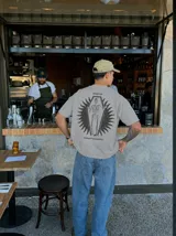 Remera gris de manga corta con corte regular, de la marca Kaboa Industries, con estampa en la espalda que presenta un esqueleto dentro de un ataúd rodeado por alas oscuras y las leyendas WAKE UP y Kaboa Industries.