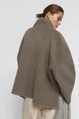 Cazadora de corte amplio confeccionada en hilatura con lana, color beige. Presenta cuello subido, manga larga y cierre frontal con botones negros. Destaca por sus acabados con costuras de hilo a contraste en los bordes.