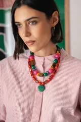 Collar corto compuesto por cuentas de cristal checo en tonos rojos de diversas formas y tamaños, con un medallón central circular de cristal checo en color verde. Incluye cadena de ajuste para regular el largo.