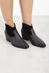 Botineta de cuero negro mate con inserciones de gamuza en el talón, punta cuadrada y tacón de bloque. Cuenta con cierre lateral interno.