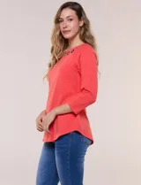 Remera blanca de algodón con elastano, de corte semi holgado, escote bote con ojalillos metálicos frontales, mangas tres cuartos raglán y ruedo asimétrico curvado.