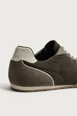 Zapatillas de estilo retro con cordones blancos, capellada marrón combinada con paneles de gamuza gris y detalles en cuero. Suela de goma a contraste.