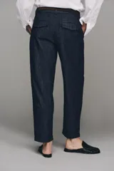 Pantalón chino de tiro bajo color marrón oscuro, con pernera recta y bajo con vuelta. Incluye un cinturón trenzado delgado de color marrón claro. Cuenta con bolsillos delanteros y cierre frontal con cremallera y botón.