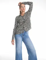Camisa de manga larga con cuello solapa y cierre frontal de botones. Presenta un diseño estampado con patrón de cebra en tonos blanco y negro, puños abotonados y ruedo redondeado.