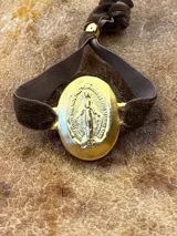 Pulsera elástica de terciopelo marrón con medalla ovalada dorada de la Virgen María.