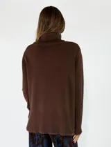 Sweater de cuello alto en color beige, con diseño de punto liso y terminaciones acanaladas en puños y ruedo. Presenta aberturas laterales en el bajo y un detalle de borde desflecado en el ruedo y los puños.