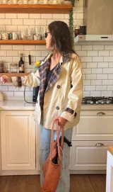 Campera tipo trench corta de gabardina color beige, con diseño de doble botonadura y solapas con forro interior a cuadros. Presenta mangas largas con puños ajustables y corte holgado.