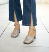 Zapato de cuero vacuno color gris topo, con talón descubierto y pulsera con hebilla. Tiene taco de madera forrado en cuero y suela de goma. La horma es de punta cuadrada, ancha y cómoda.