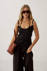 Top de punto negro con diseño acanalado vertical, escote redondo pronunciado y tirantes anchos con detalle de perlas o cuentas decorativas.