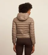 Campera puffer deportiva de mujer, confeccionada en tejido tecnológico ligero con relleno acolchado. Presenta capucha integrada, cierre frontal con cremallera y diseño de manga larga. La prenda destaca por su versatilidad, siendo capaz de transformarse en una pequeña cartera.