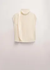 Blusa de seda color blanco marfil, con cuello alto drapeado y detalle de bufanda integrada al cuello. De manga larga con puños ajustados mediante tiras.