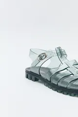 Sandalias jelly color gris translúcido, con diseño entrecruzado y hebilla lateral ajustable.