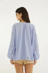 Blusa celeste de algodón con bordado calado y ojales en el delantero, mangas amplias y ruedo. Presenta escote redondo con cierre frontal de botones.