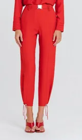 Pantalón rosado de tiro alto con cintura estructurada y hebilla metálica decorativa, diseño fluido de corte relajado con pliegues frontales y ajuste con cordón en los tobillos.