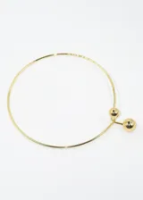 Gargantilla rígida dorada con dos esferas decorativas, una más grande que la otra, unidas por una barra vertical.