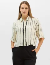 Camisa de corte holgado y silueta recta, con estampado de rayas verticales irregulares en color negro sobre fondo crema. Presenta cuello camisero clásico, mangas cortas amplias y cierre frontal con botones.