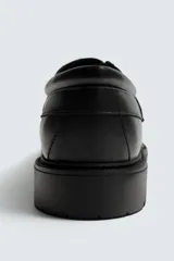 Zapato tipo náutico color negro, con parte superior lisa, bordón y horma redonda. Cuenta con suela de volumen y piso track.