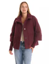 Tapado de tejido bouclé color marrón, con silueta evasé y largo a la cadera. Presenta cuello alto envolvente, cierre frontal oculto con botones a presión y bolsillos frontales de gran tamaño. Sus mangas son 3/4 con corte amplio y puños de tejido rib al tono que se extienden para cubrir las muñecas.