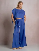 Pantalón palazzo de lino color azul, de tiro alto con cintura elastizada y cinto lazo incorporado con cuentas decorativas en las puntas. Presenta aberturas laterales pronunciadas en las piernas y corte amplio.