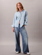 Camisa de corte clásico con estampado de rayas verticales en tonos celeste y amarillo. Presenta cuello en punta, mangas largas con hombros caídos y cierre frontal mediante botones.