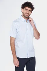 Camisa de manga corta color celeste claro, con cuello abotonado (button-down) y un bolsillo de parche en el pecho.