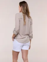 Blusa de calce relajado color salmón, confeccionada en tela liviana con textura sutil. Presenta escote en V con abotonadura frontal, bolsillo parche en el pecho, mangas largas regulables con presilla y ruedo con opción de anudar en el frente.