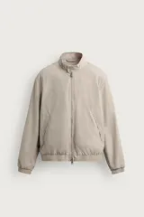 Cazadora regular fit de tejido técnico color beige, con cuello subido, cierre de botones y cremallera frontal, bolsillos de doble vivo en la cadera y acabados elásticos.