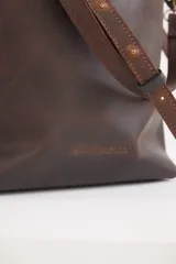 Cartera tipo shopper de cuero color suela, con diseño minimalista, correa larga ajustable y herrajes metálicos en tono bronce.