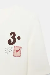 Camiseta de manga corta color blanco, con cuello redondo y bajo recto. Presenta un pequeño bordado y estampado en el pecho, incluyendo el número "3." y un pequeño cuadrado con un corazón.