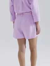 Short de lino en color crudo, de corte recto y tiro medio. Presenta una cintura con pasacintos y un cordón trenzado decorativo con borlas en el frente.