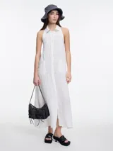 Vestido largo blanco de lino, sin mangas, con cuello camisero y escote halter. Presenta espalda descubierta con ajuste regulable y bordado tipo pespunte en contraste sobre el cuello.