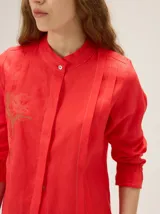 Camisa de lino color crudo, con cuello mao y cierre frontal con botones. Cuenta con detalles de alforzas verticales y diseño bordado floral en el frente, además de mangas 3/4 con volumen y puños elásticos.