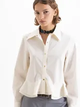 Camisa blanca de popelina con ajuste al cuerpo, puños anchos, cuello de puntas largas, broches dorados y doble volado en la cintura.