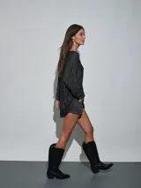 Short de jean blanco con tachas doradas decorativas en los bolsillos delanteros y en los laterales, talle medio y cierre frontal con botón y cremallera.