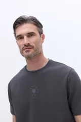 Remera de algodón con textura, cuello redondo y calce regular. Presenta un diseño minimalista con una estampa circular sutil en el centro del pecho.