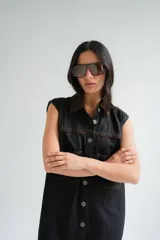 Vestido corto de jean color gris oscuro con efecto acid wash, sin mangas, con cuello camisero y cierre frontal de botones. Incluye dos bolsillos en el pecho con solapa y pespuntes decorativos.