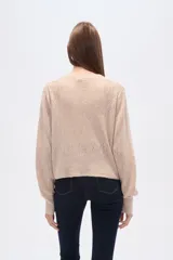 Cárdigan color beige de poliéster con cuello en V, corte al cuerpo y mangas abullonadas. Decorado con cuentas blancas.